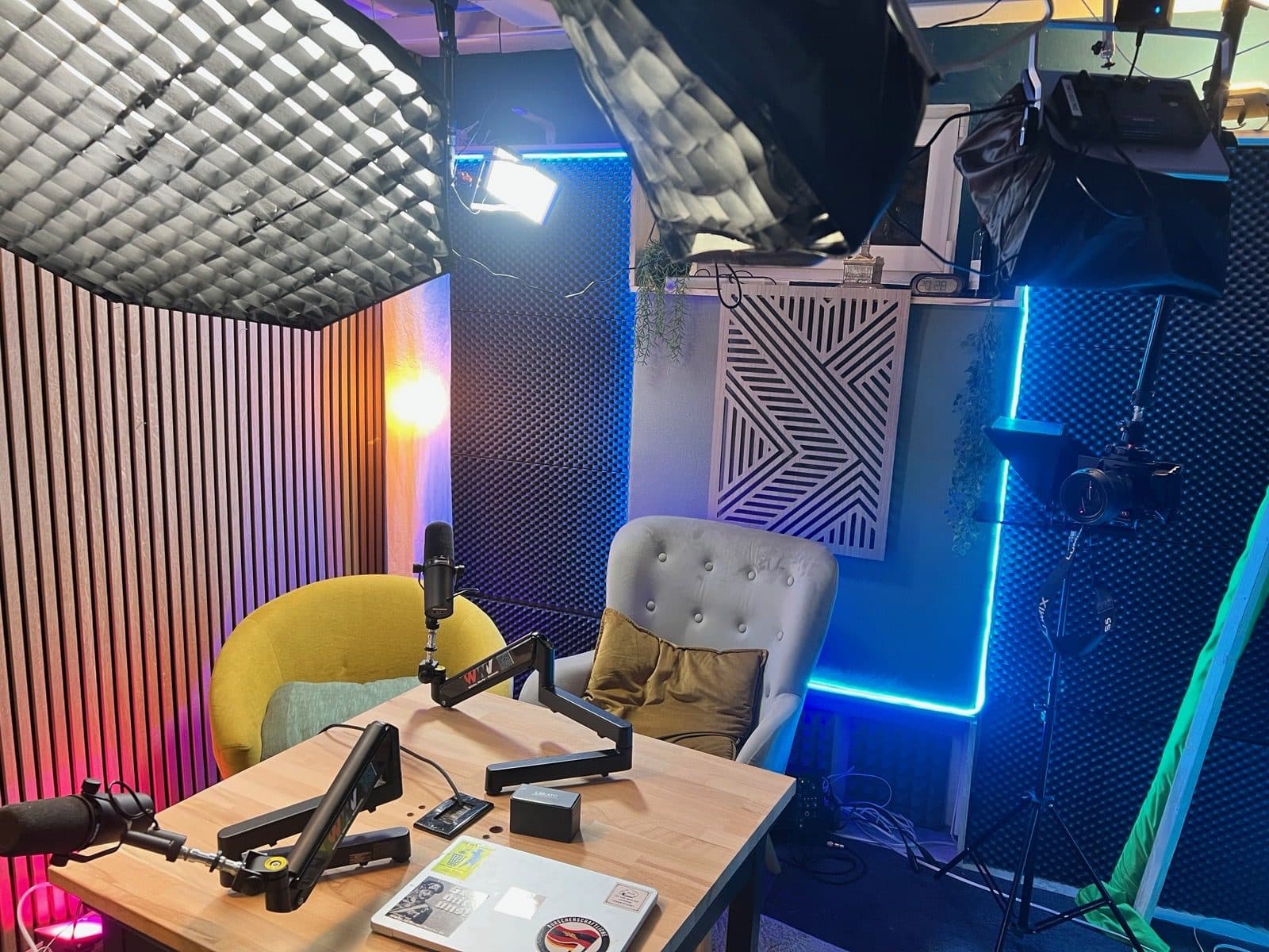 Das Askalon-Podcast-Studio: Tisch mit zwei Mikrofonen, zwei Sessel, Softboxen und LED-Licht